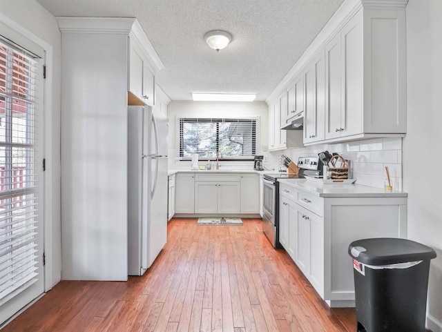 kitchen with freestanding refrigerator, stainless steel range with electric cooktop, decorative backsplash, light countertops, and light wood-type flooring