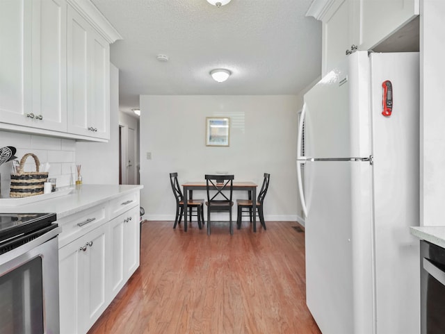 kitchen featuring decorative backsplash, light countertops, white cabinets, and freestanding refrigerator