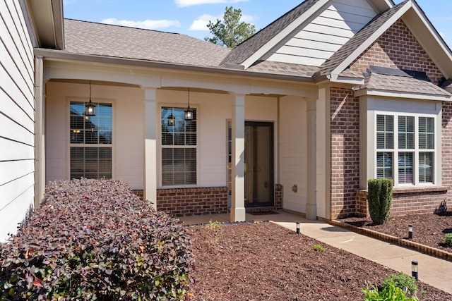 entrance to property featuring brick siding and a shingled roof