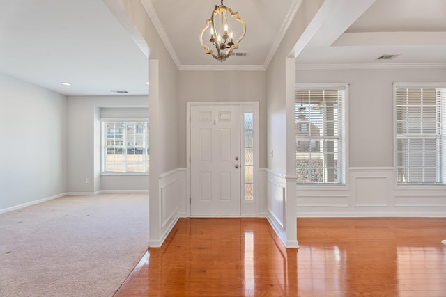 entrance foyer with a wainscoted wall, visible vents, light wood-style flooring, ornamental molding, and a chandelier