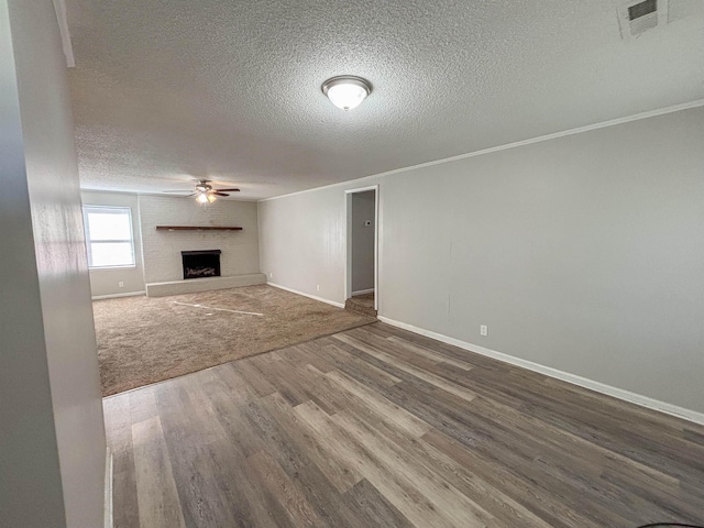 unfurnished living room with visible vents, a large fireplace, baseboards, wood finished floors, and a ceiling fan