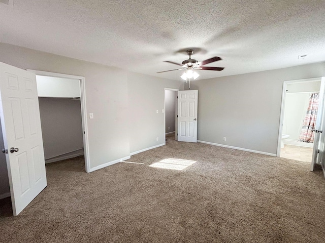 unfurnished bedroom featuring a walk in closet, baseboards, carpet, ensuite bathroom, and a textured ceiling