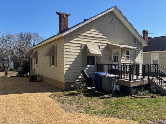 back of property with a yard, central AC, a wooden deck, and a chimney