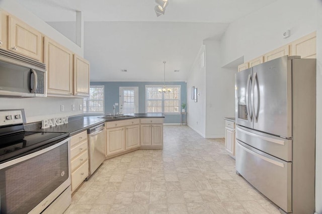 kitchen with light brown cabinets, a peninsula, a sink, appliances with stainless steel finishes, and dark countertops