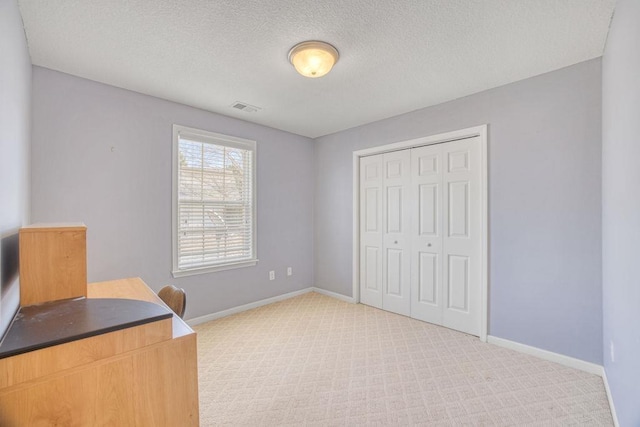 unfurnished office with a textured ceiling, baseboards, visible vents, and light carpet