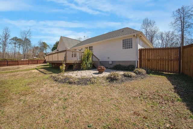 rear view of house with a fenced backyard, a yard, a fire pit, and a deck