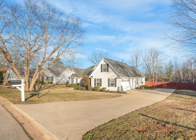 view of front of home with an attached garage, concrete driveway, a front lawn, and fence