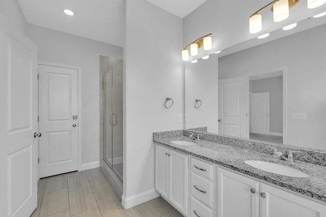 bathroom with double vanity, baseboards, a stall shower, and a sink