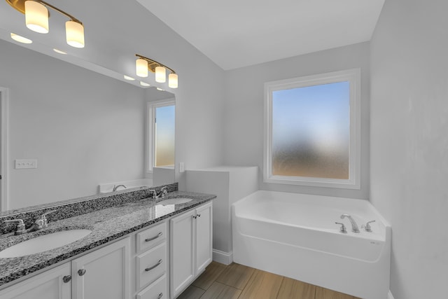 bathroom featuring a garden tub, wood finished floors, double vanity, and a sink