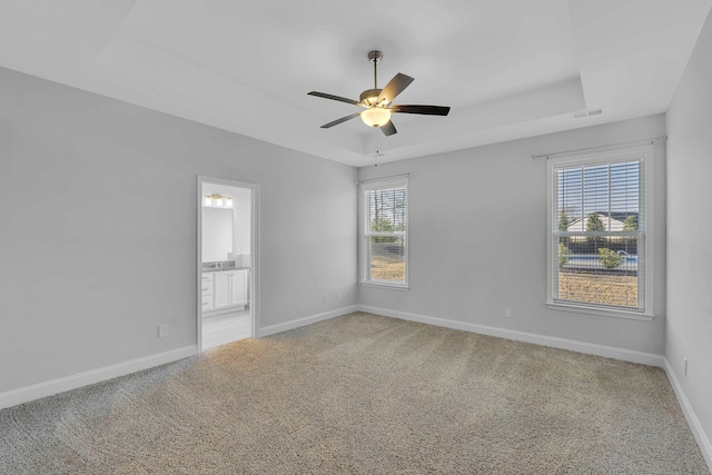 spare room with a ceiling fan, visible vents, baseboards, a tray ceiling, and light carpet