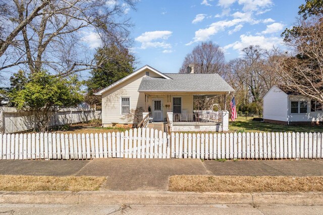 view of front of property with covered porch, a fenced front yard, and a shingled roof