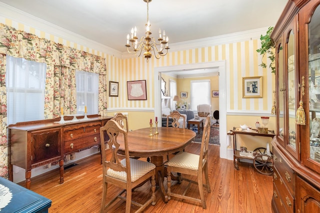 dining space with a chandelier, wallpapered walls, crown molding, and light wood-style floors