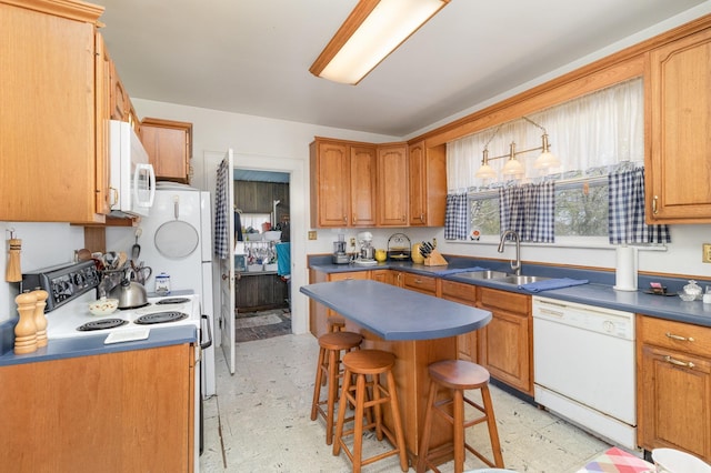 kitchen featuring dark countertops, light floors, a kitchen breakfast bar, white appliances, and a sink