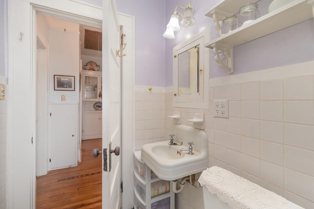 half bath featuring wood finished floors, wainscoting, tile walls, and a sink