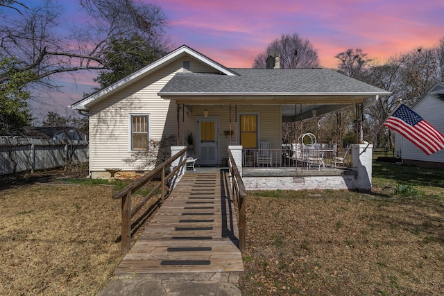 bungalow-style house featuring a patio, a front lawn, fence, and a shingled roof