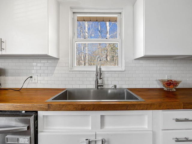 kitchen with wood counters, tasteful backsplash, white cabinetry, and a sink