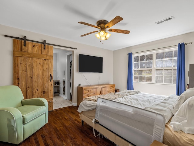 bedroom with visible vents, dark wood-type flooring, a ceiling fan, ensuite bath, and a barn door