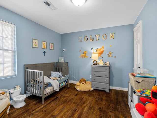 bedroom with visible vents, a nursery area, wood finished floors, and baseboards