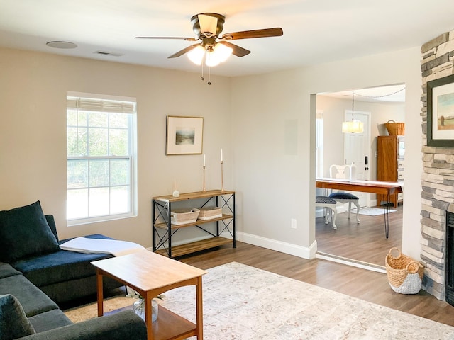 living room with wood finished floors, a fireplace, baseboards, and ceiling fan