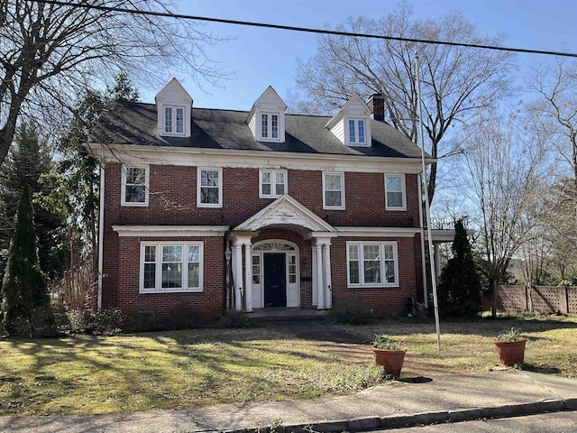 view of front of property with brick siding, a chimney, a front yard, and fence