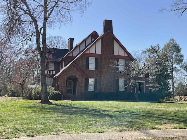 english style home featuring brick siding, a front yard, and a chimney