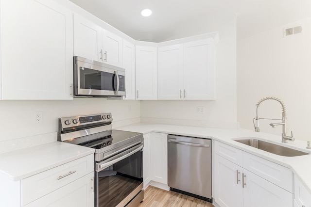 kitchen featuring visible vents, light wood-style flooring, white cabinets, stainless steel appliances, and a sink