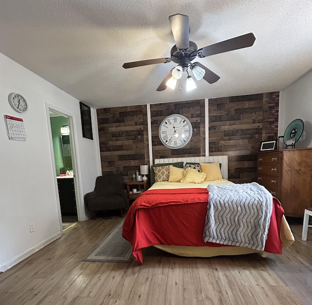 bedroom featuring a textured ceiling, ensuite bath, wood finished floors, wooden walls, and ceiling fan