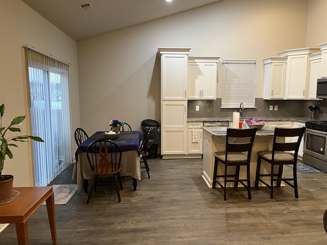 kitchen with a breakfast bar, stainless steel appliances, dark wood-type flooring, tasteful backsplash, and a center island