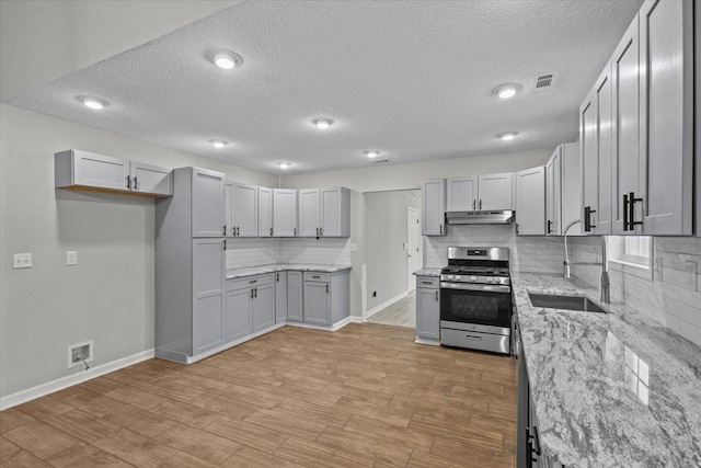 kitchen featuring light stone countertops, gas stove, visible vents, a sink, and under cabinet range hood