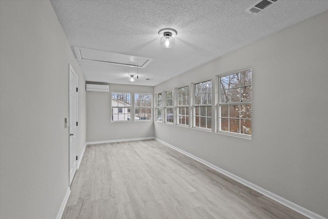 spare room featuring visible vents, wood finished floors, a wall unit AC, baseboards, and attic access