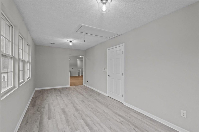 unfurnished room with attic access, wood finished floors, baseboards, and a textured ceiling