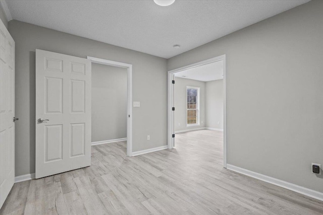 unfurnished bedroom featuring a textured ceiling, light wood-type flooring, and baseboards