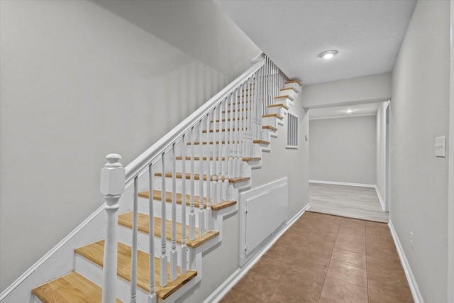 staircase featuring tile patterned floors, a textured ceiling, and baseboards