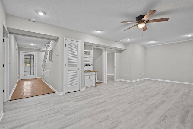 below grade area with stairs, light wood-style flooring, a ceiling fan, and baseboards