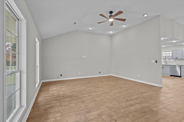 empty room with light wood-type flooring, a ceiling fan, a sink, baseboards, and lofted ceiling