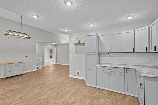 kitchen with light stone countertops, baseboards, light wood finished floors, decorative light fixtures, and tasteful backsplash