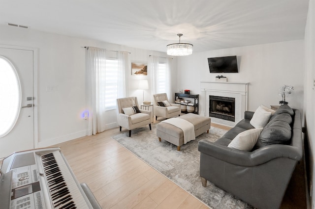 living area with baseboards, visible vents, light wood finished floors, an inviting chandelier, and a fireplace with flush hearth