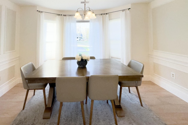 dining room featuring visible vents, a decorative wall, wainscoting, light wood-style floors, and a notable chandelier