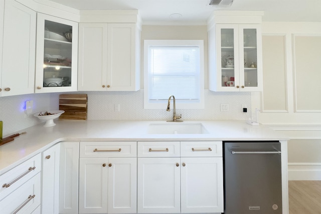 kitchen featuring tasteful backsplash, white cabinets, dishwasher, and a sink