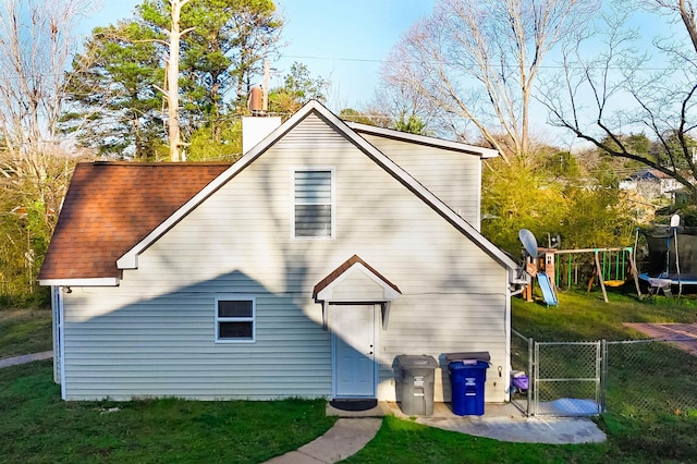 rear view of property featuring a gate, fence, a playground, a trampoline, and a lawn