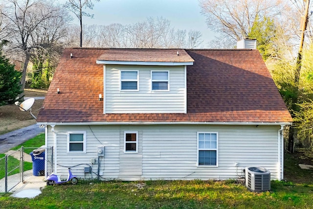 back of house featuring fence, central AC unit, a chimney, and a shingled roof