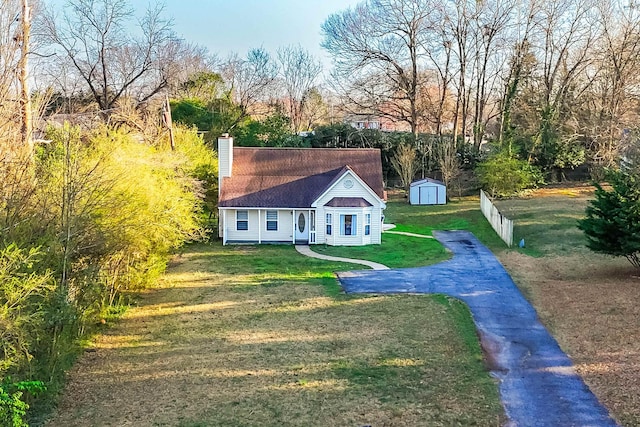 view of front of home with fence, a shed, a front yard, a chimney, and an outbuilding