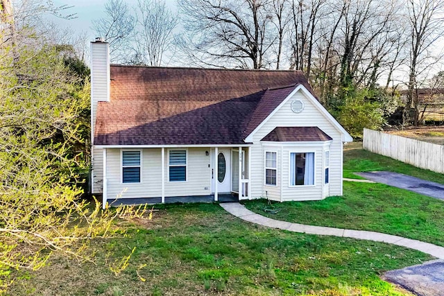 view of front facade with fence, a chimney, a front yard, and a shingled roof