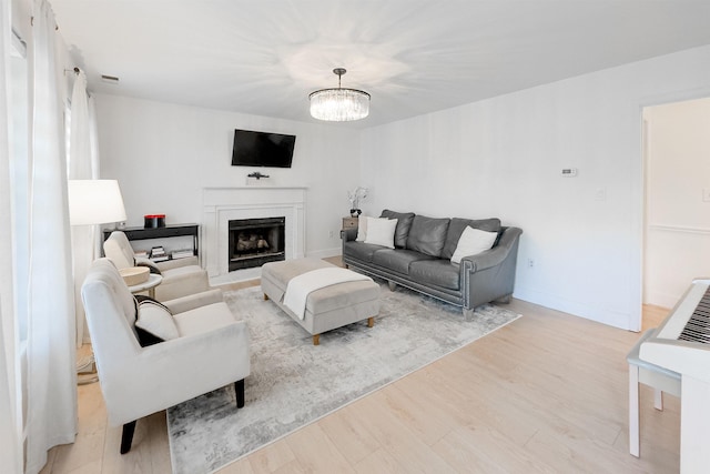 living room with light wood finished floors, a notable chandelier, baseboards, and a fireplace with flush hearth