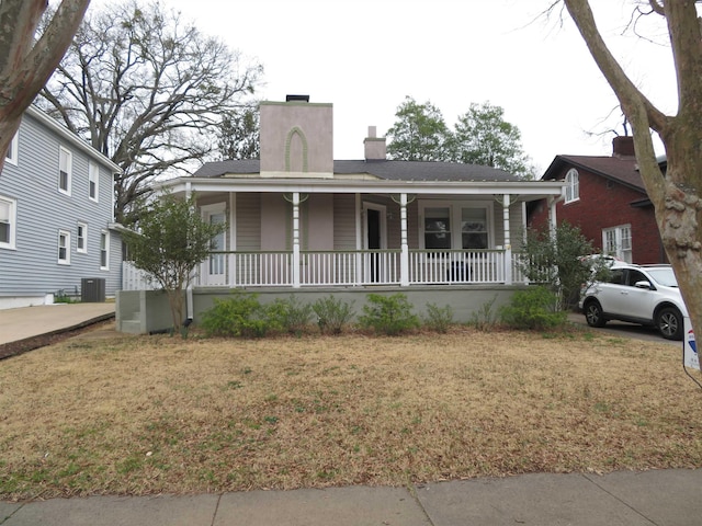 view of front of home featuring central air condition unit, a front yard, covered porch, and a chimney