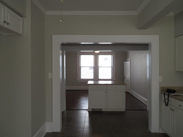 kitchen with a center island, crown molding, baseboards, white cabinetry, and dark tile patterned flooring