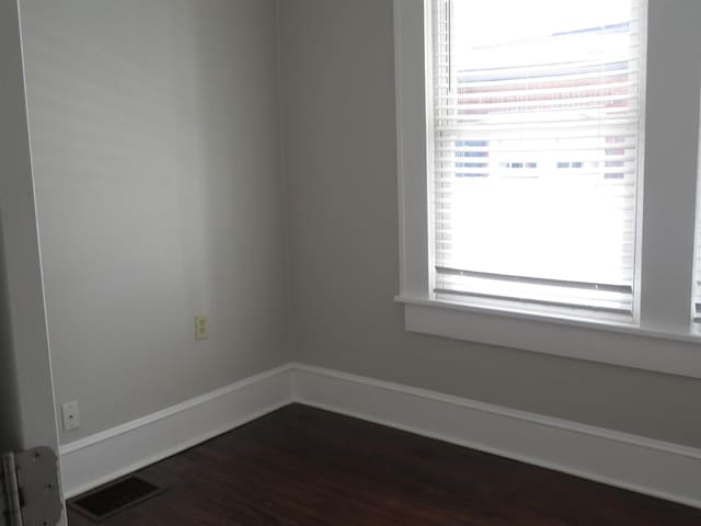 empty room with visible vents, baseboards, and dark wood-type flooring