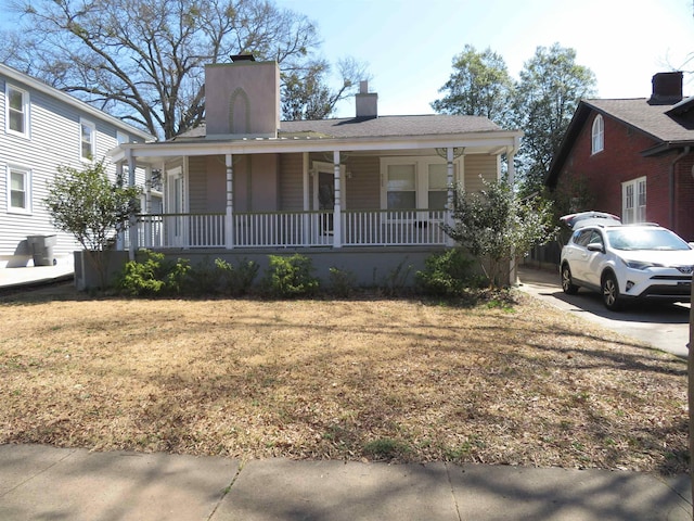 view of front of home featuring covered porch, a chimney, and roof with shingles