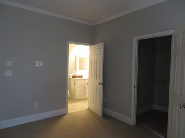 unfurnished bedroom featuring a closet, carpet, crown molding, baseboards, and a spacious closet