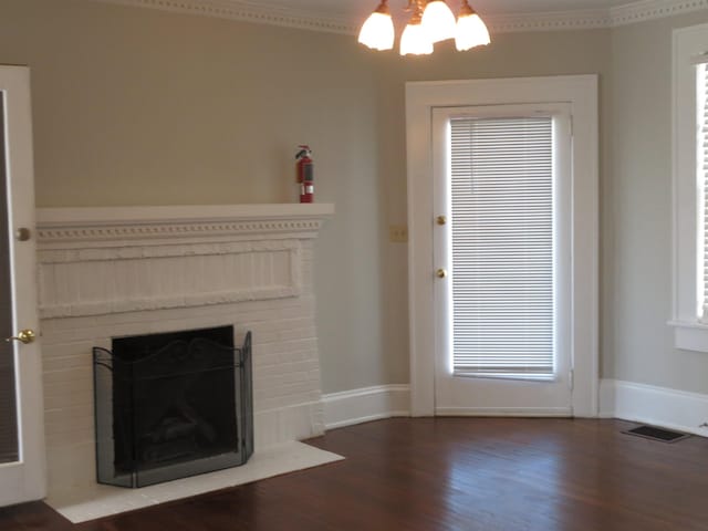 unfurnished living room with visible vents, wood finished floors, an inviting chandelier, a fireplace, and crown molding